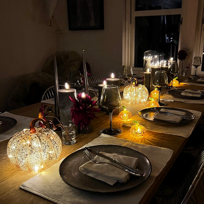 A set of orange mini pumpkin-shaped LED lights placed on a table with lit candles, creating a warm and cozy ambiance.